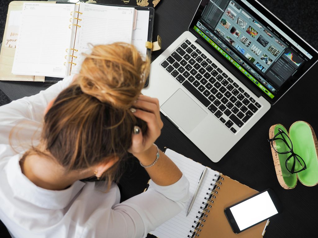A woman sitting by a laptop, with the hands on her facce looking stressed